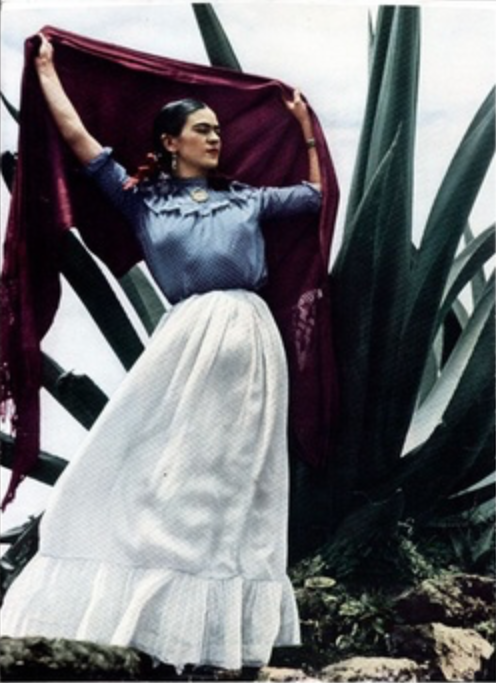 Frida Kahlo holding up her shawl to catch the wind posing with large Mexican plant