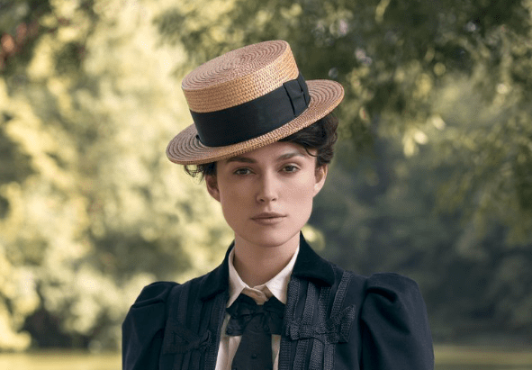 Keira Knightley as Colette standing in park looking into the camera wearing straw boater hat